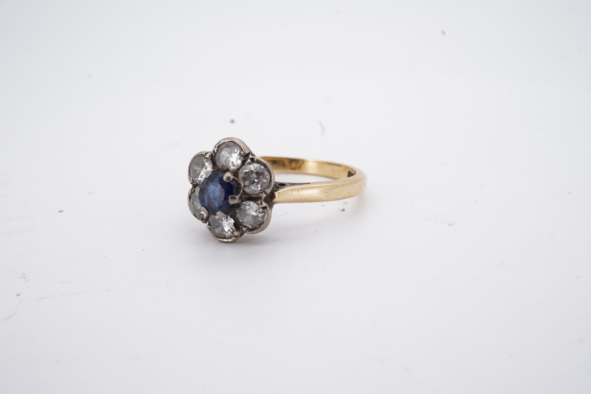 An early to mid 20th century yellow metal (stamped 18ct), singe stone sapphire and six stone diamond set circular cluster ring, size O, gross weight 3.7 grams.